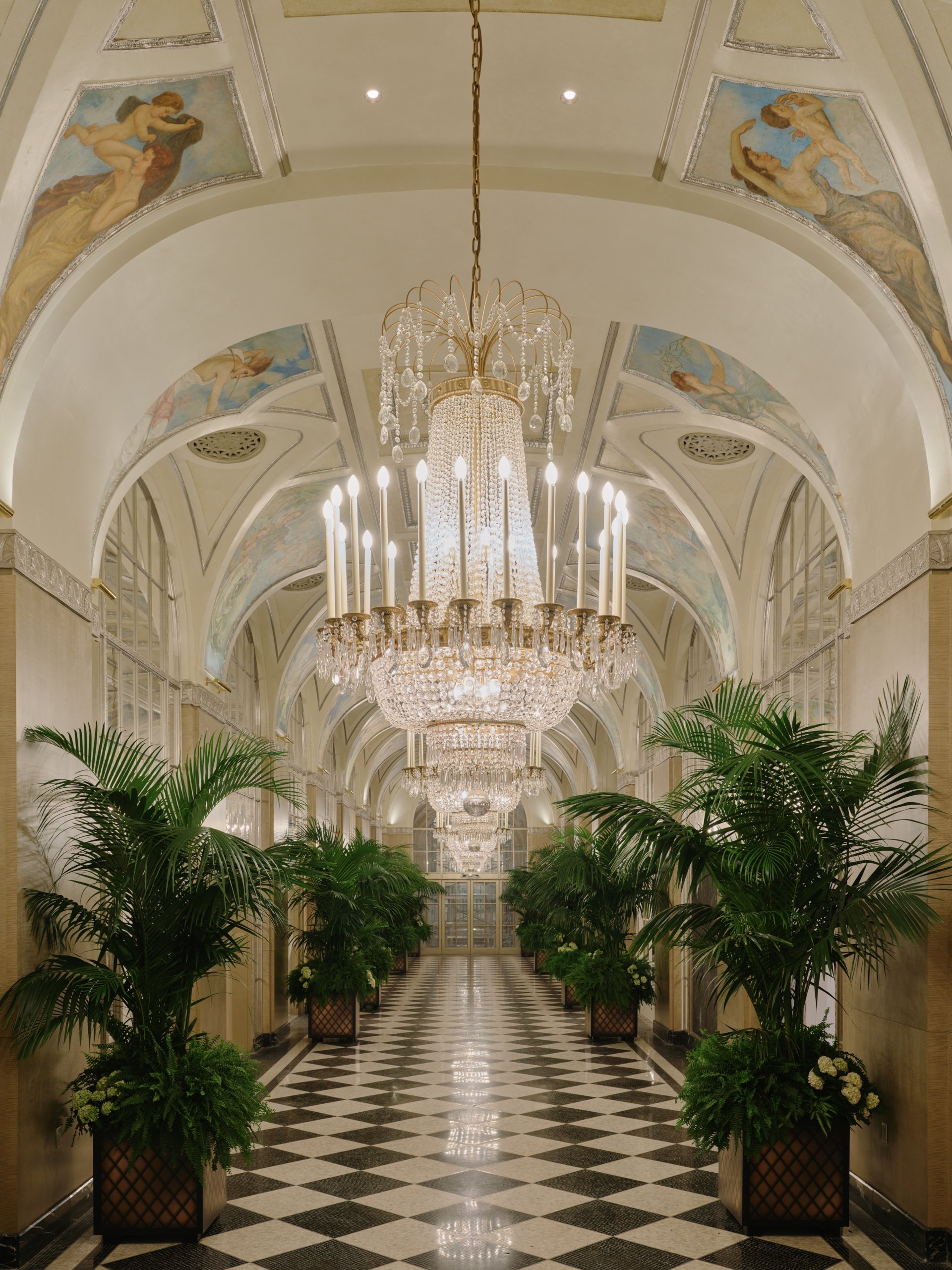 the silver corridor lit up with green trees in the front below the chandelier