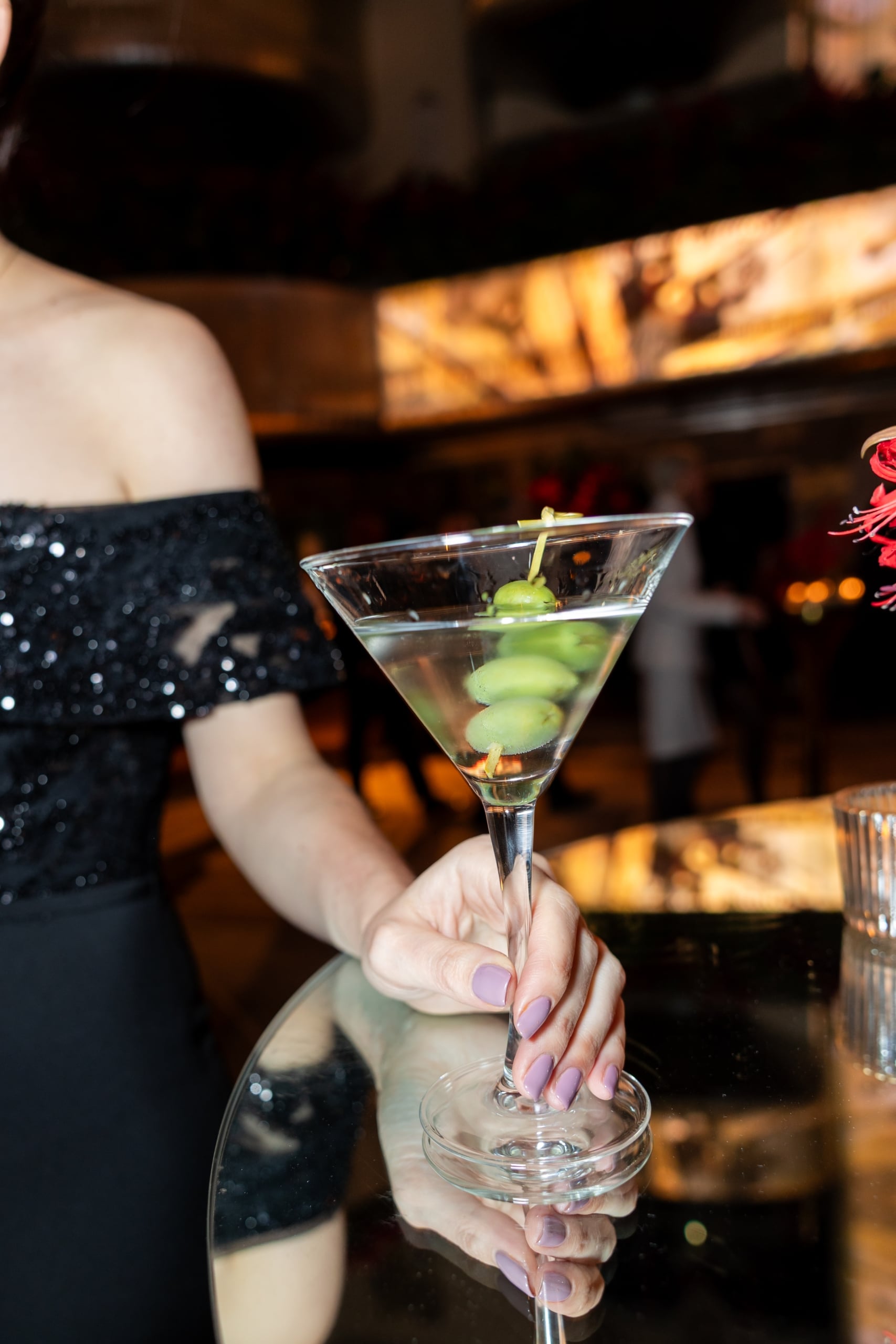 una persona que sostiene una copa de martini con aceitunas verdes dentro