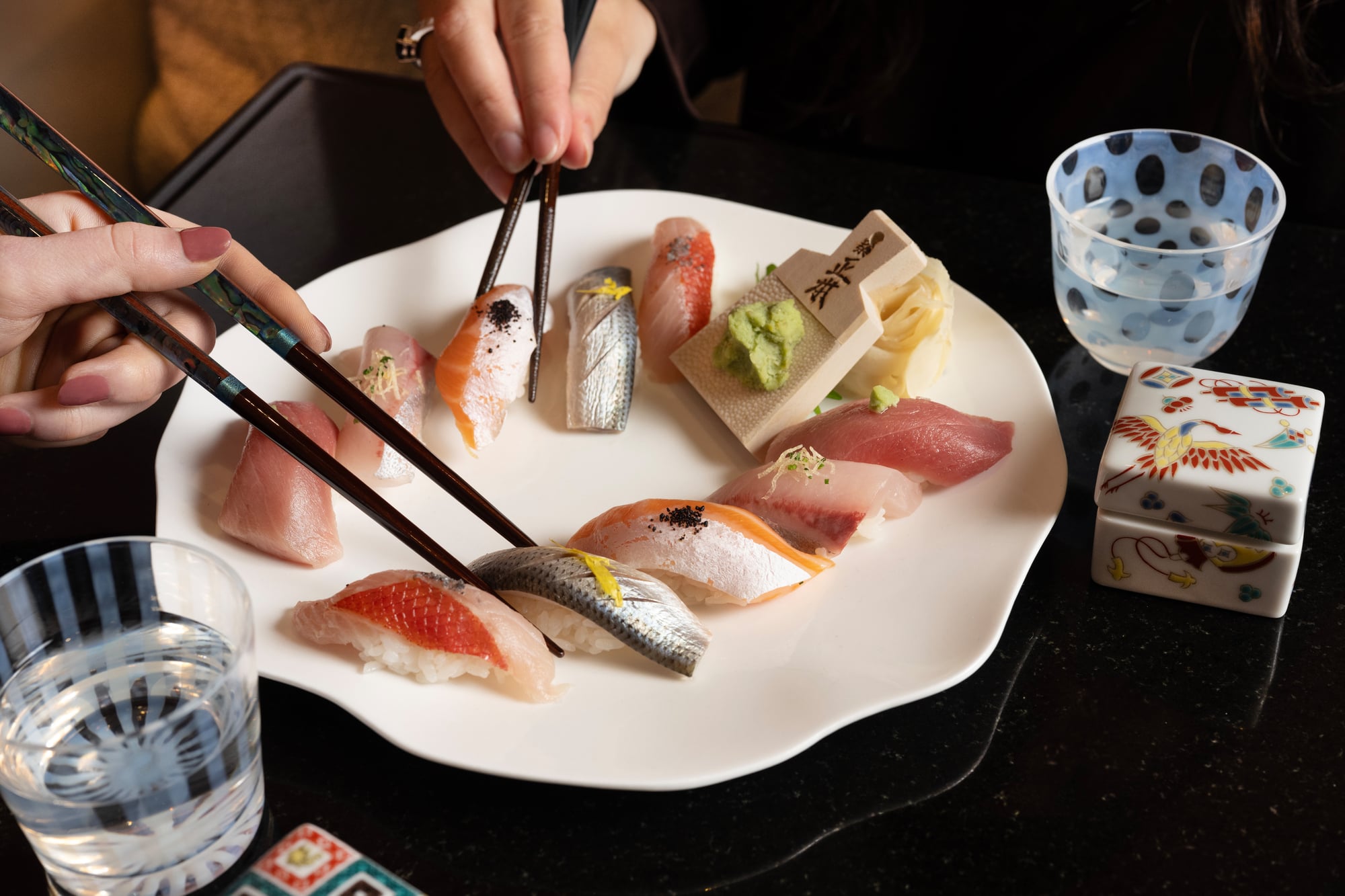 un plat de sushis devant lequel deux personnes utilisent des baguettes pour prendre des morceaux